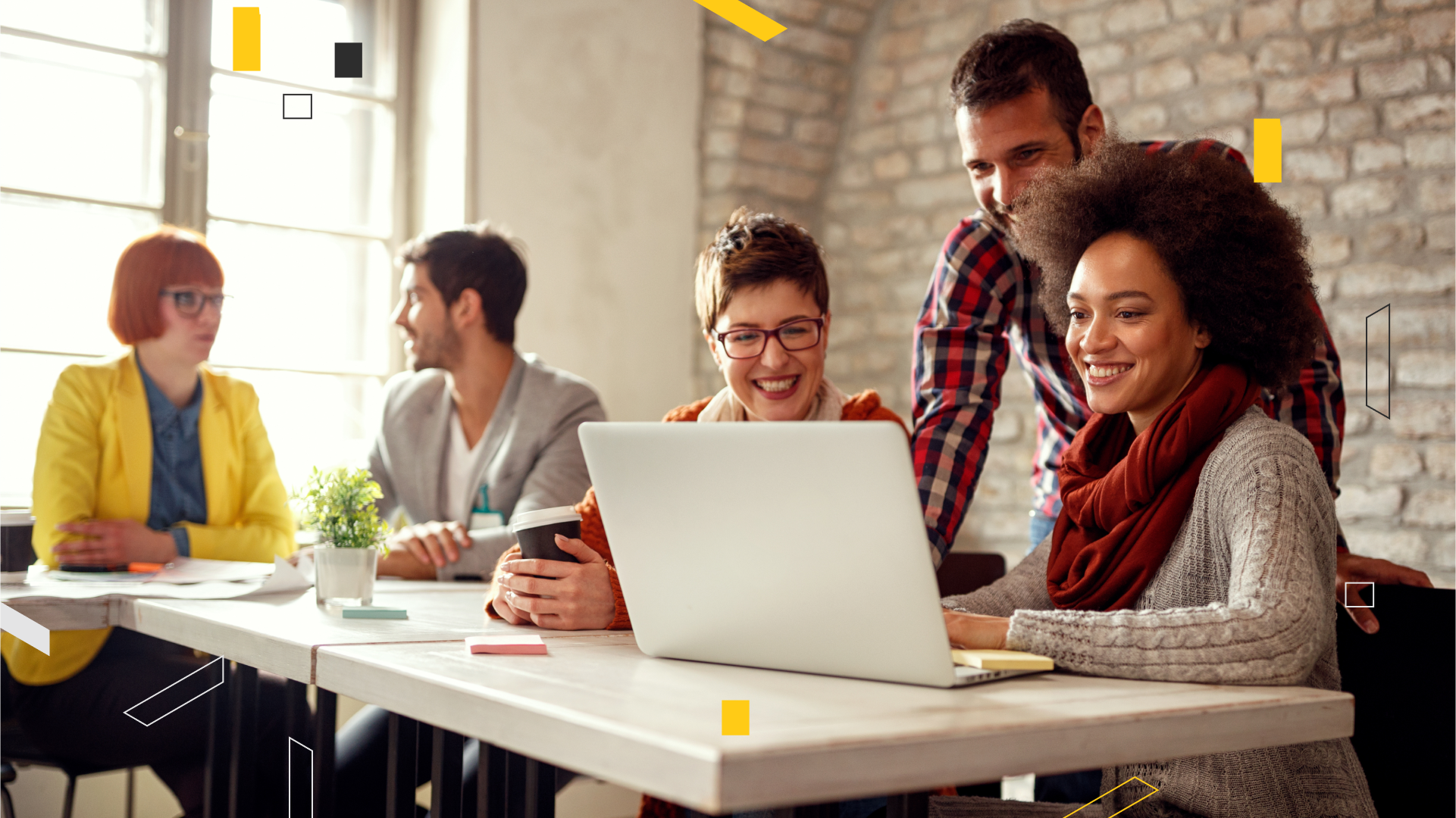 employees chatting at a desk overlooking a laptop